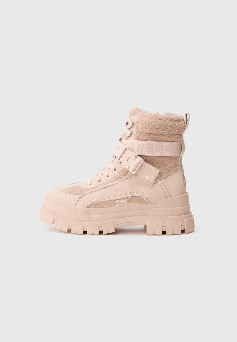 Botines gruesos hasta el tobillo en beige suave, con parte superior de forro polar, detalles en cuero, mezcla de texturas y suela con grueso dibujo para tracción.