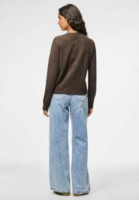 Maglione marrone a maglia con scollo rotondo, abbinato a jeans a gamba larga di un blu chiaro. I jeans presentano una texture sbiadita e tasche posteriori.
