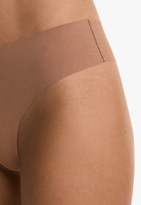 Beige naadloze onderkleding met een gladde, matte textuur en brede tailleband. De stof is rekbaar, zonder zichtbare naden of versieringen.