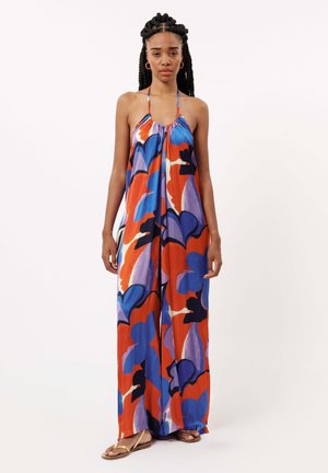 Robe maxi en tissu léger avec un col halter et un motif floral audacieux en rouges, bleus et violets. Des sandales plates complètent le look.