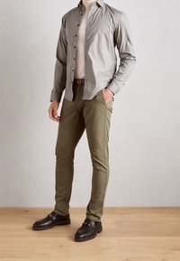 Košile na knoflíky v světle šedé s malými námořnickými puntíky, v kombinaci s olivově zelenými přiléhavými kalhotami a černými koženými mokasíny se zlatými akcenty.