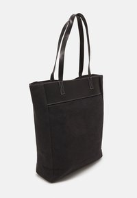 Bolsa de lona negra con largas asas de cuero negro y detalles de costura blanca, que presenta una forma estructurada y una textura suave.
