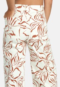 Blumenmuster-Hosen in Creme mit rostfarbenen Blättermotiven. Verfügt über Seitentaschen und ein lässiges Passformdesign. Robuster Baumwollstoff.