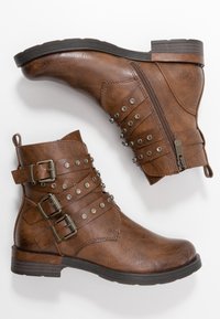 Stivali ankle in pelle marrone con punta arrotondata, borchie decorative in argento, tre fibbie e una cerniera laterale. Superiori testurizzati con tacco basso impilato.