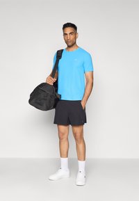 Blaues T-Shirt mit kurzen Ärmeln, schwarze Shorts, weiße Sneakers und eine schwarze Sporttasche. Glatter Stoff, lässige Passform, vor einem neutralen Hintergrund präsentiert.