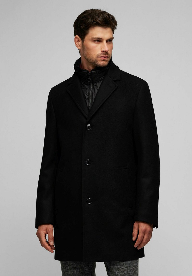 Abrigo de mezcla de lana negro con un cuello estructurado, tres botones y una tapa de cremallera oculta. Cuenta con bolsillos laterales y una textura suave.
