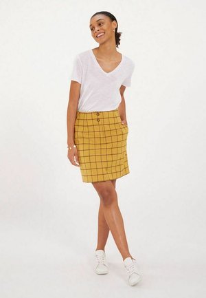 Jupe jaune à carreaux avec une coupe droite, comportant deux boutons à l'avant et des poches latérales. Associée à un t-shirt blanc à col en V et des baskets.