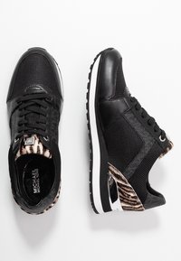 Baskets athlétiques noires avec tige en mesh et cuir, accents à imprimé animal, lacets plats et semelles blanches. Côtés texturés et détail du logo présents.