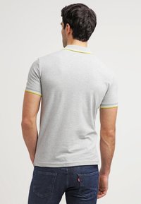 Ljusgrå kortärmad polo med en kontrasterande gul kant vid kragen och ärmarna, tillverkad av mjukt material. Har en klassisk passform.