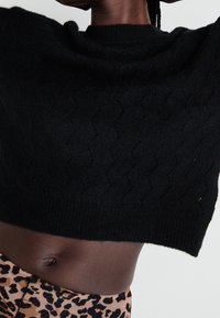 Svart kortärmad tröja i strukturerad stickning. Har en bred halsringning och en vågig mönster, kombinerad med leggings i djurtryck.