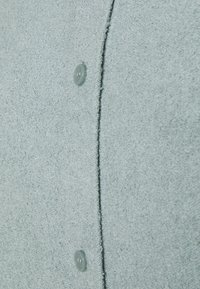 Tissu de pull bleu clair texturé avec une apparence duveteuse, présentant une rangée de boutons bleu clair sur le devant et une couture piquée.