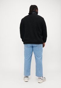 Μαύρος φλις πουλόβερ με υφή, συνδυασμένο με ανοιχτό μπλε τζιν παντελόνι ίσιας γραμμής. Γκρι αθλητικά συμπληρώνουν την εμφάνιση.