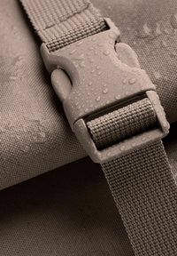 Sangle beige avec une surface texturée et une boucle étanche, présentant des gouttes d'eau, posée sur un fond en tissu similaire.