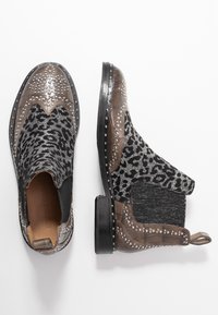 Botas Chelsea con una combinación de tela negra y estampado de leopardo, adornadas con tachuelas plateadas, y con la puntera y el tacón de cuero marrón oscuro.