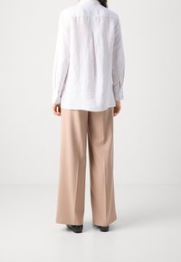 Witte linnen lange mouw shirt met een rugplooi, gecombineerd met beige wijde broek, weergegeven van achteren tegen een lichte achtergrond.