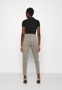 Camisa polo preta combinada com calças xadrez de alta cintura em bege e cinza. As calças apresentam um ajuste afunilado e bolsos traseiros.