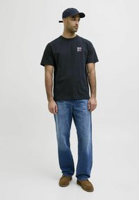 Sort bomulds t-shirt med et lille logo foran, parret med lys blå lige ben jeans og brune ruskind loafers, toppet med en marineblå kasket.