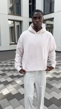 Moleton rosa claro com um bolso na frente e cordão ajustável, combinado com calças cream tapered sobre uma superfície externa com padrão.