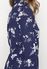 Mörkblå blommig klänning med vita mönster, som har krage, långa ärmar och midjebälte för en definierad form.