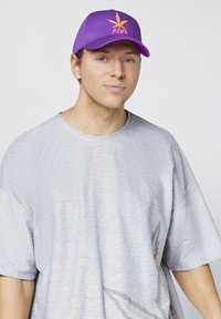 Purple baseball cap with green and pink leaf design and "SUGAR" text; gray oversized t-shirt with subtle pattern.