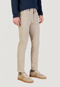 Pantalones chinos de algodón beige con corte slim, cierre de cremallera y bolsillos laterales, combinados con zapatillas de color beige claro con detalles de ante y cordones blancos.