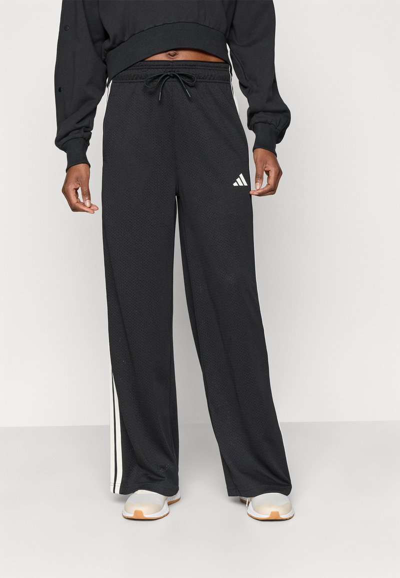 Čierne športové nohavice s textúrou z oka, elastickým pásom, šnúrkou a bielymi pruhmi po stranách. Na ľavom stehne sa nachádza logo Adidas.