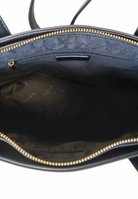 Interno di una borsa a mano in pelle nera con una texture liscia, chiusura con zip dorata e tasca con zip. Foderata con un tessuto scuro che presenta un marchio discreto.