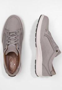 Chaussures de sport en cuir gris avec une tige souple, des panneaux latéraux perforés et une semelle blanche avec des accents noirs. Lacets et détail de couture décorative.