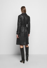 Black leather trench coat with a belted waist, long sleeves, and a classic collar. Smooth texture with a straight-cut design.