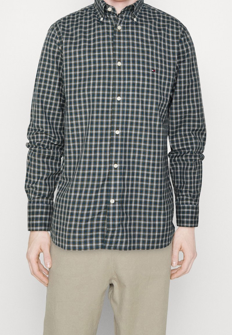 Camisa de botones en verde oscuro con un estampado de cuadros en blanco y azul claro. Cuenta con un collar abotonado y mangas largas.