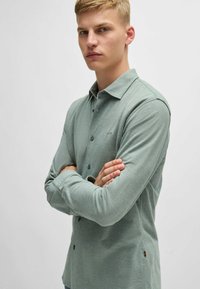 Lichtgroen overhemd met lange mouwen, knoopsluiting aan de voorkant, een effen textuur en een klein logo op de borst. Voorzien van een klassieke kraag en knoopmanchetten.