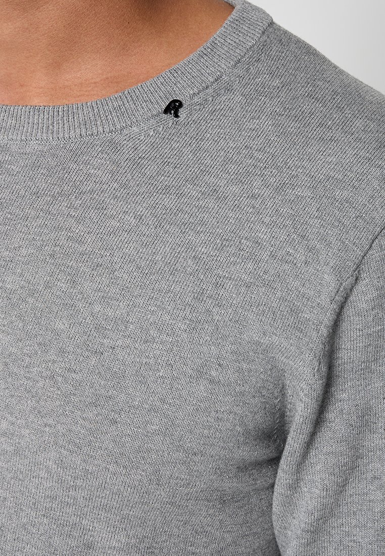 Grauer Strickpullover mit einem gerippten Rundhalsausschnitt, versehen mit einem kleinen schwarzen Logo-Akzent nahe der Schulter, glatter Textur und taillierter Passform.