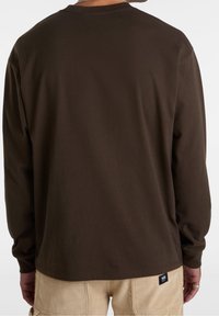 Braunfarbiges Langarm-T-Shirt mit rundem Halsausschnitt, glatter Textur und einem kleinen Markenetikett am Saum. Die Rückansicht zeigt die Details der Ärmel und des Saums.