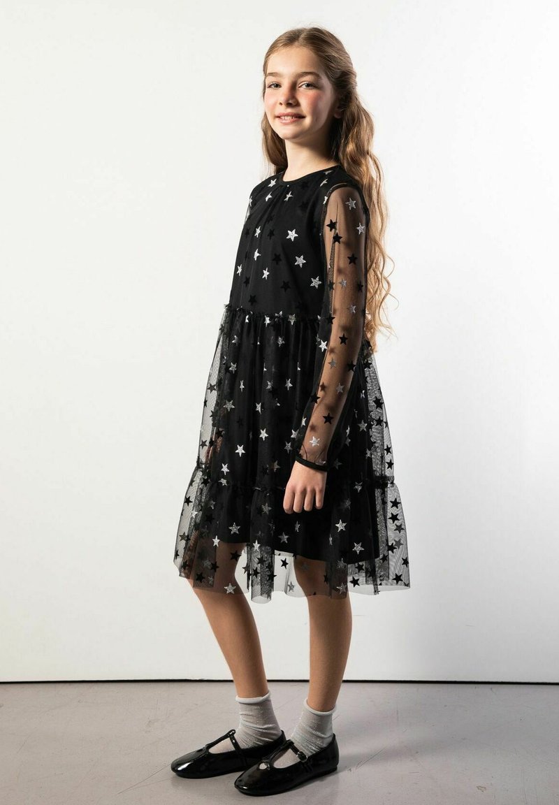 Czarna sukienka z wzorem gwiazd, przezroczystymi długimi rękawami, falbanianym dołem i dopasowanym gorsetem. Noszona z czarnymi butami i szarymi skarpetkami.