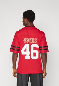Sarkans futbola krekls ar melnām svītrām. Tam ir uzraksts "49ERS" zeltā un "46" baltā krāsā. Īsas piedurknes un apaļais kakla izgriezums.