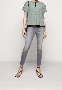 Jasnozielony krótki top z dekoltem typu keyhole, w połączeniu z dopasowanymi szarymi dżinsami i czarnymi sandałami na paski. Prosty wzór i miękka tkanina.