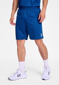 Shorts de sport bleus avec une taille élastique, en tissu lisse. Présente un logo blanc au bas et est assorti avec des chaussettes et des chaussures blanches.