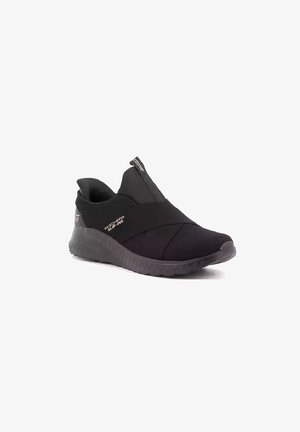 Sneaker nera slip-on con suola testurizzata, cinghie elastiche incrociate e linguetta, etichettata "Skechers Slip-Ins" sul lato.
