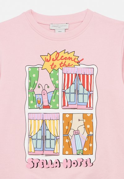 Rosa skjorte med fire vindusillustrasjoner som viser gardiner, to tegneserieinsekter, og teksten "Velkommen til Stella Hotel" i fargerik skrift.