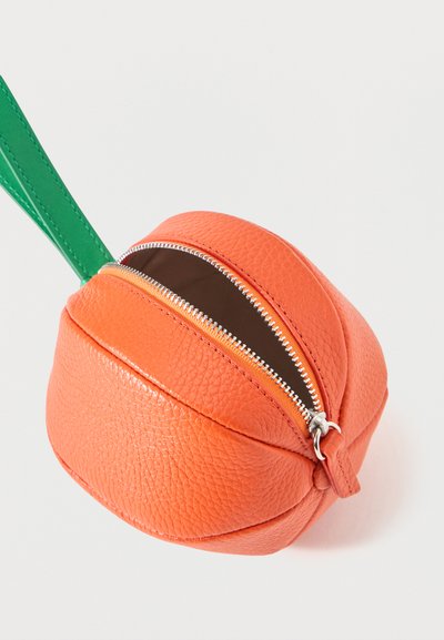 Pochette ronde en cuir orange avec fermeture éclair, surface texturée et bracelet vert, montrée partiellement ouverte sur un fond blanc.