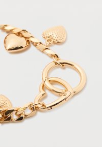 Zlatna narukvica od lanca s uvijenim karikama, srčanim privjescima i kopčom. Glatka tekstura sa sjajnom završnom obradom i različitim oblicima privjesaka.