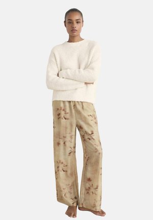 Suéter acogedor de felpa color crema combinado con pantalones de pierna ancha en tonos marrones con un patrón floral. Ambas prendas ofrecen una silueta relajada.