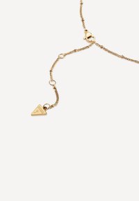 Halskette aus goldfarbener Kette mit einem dreieckigen Anhänger. Besitzt geflochtene Glieder und einen Krokodilhakenverschluss. Anhänger graviert mit "GUESS." Glatte Oberfläche.