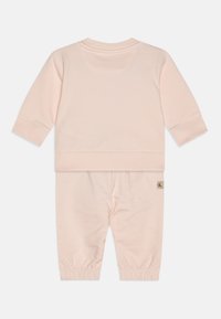 Conjunto de sudadera y pantalones de algodón de color rosa claro. La sudadera tiene mangas largas y puños acanalados; los pantalones tienen tobillos elasticados y un bolsillo trasero.