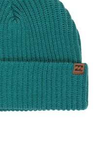 Stickad teal-färgad mössa med ribbad textur och en vikbar bård. Har en brun läderpatch med en våglogotyp framtill.
