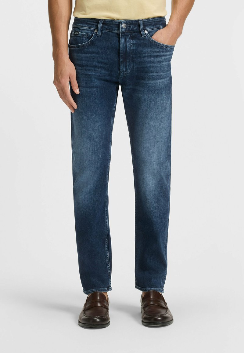 Blå denimjeans med rak passform, med framfickor, minimal urtvining och en klassisk femficksdesign. Bruna skor kompletterar looken.