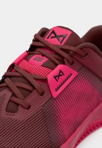 Close-up of maroon and pink athletic shoe with laces, mesh fabric, and black logo on pink tags near tongue and side.