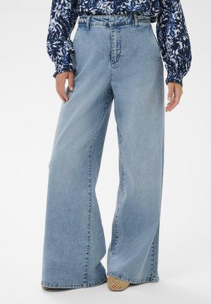 Hellblaue, hochtaillierte Jeans mit weitem Bein aus Denim, mit glatter Textur und dezentem Verblassen, kombiniert mit einem gemusterten Oberteil.