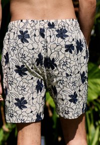 Kurze Hose mit Blumenmuster, hellbeige mit marineblauer Stickerei. Verfügt über einen elastischen Bund und zwei Gesäßtaschen. Strukturierter Stoff.