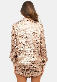 Giacca in paillettes rosa oro con vestibilità rilassata, copertura completa sul retro e paillettes circolari lucenti che creano una superficie texturizzata.